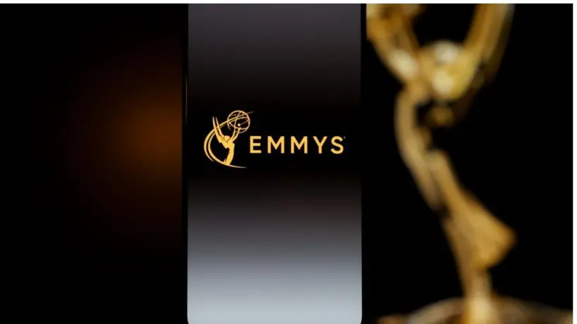 Emmys logo displayed on a smartphone screen with a blurred gold award statuette in the background^ television industry awards and digital streaming concept. Kaunas^ Lithuania - 2026 March 24