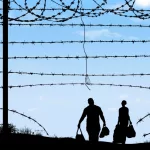 A man and woman in silhouette heading through broken border fence on the southern border of the USA.