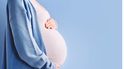 pregnant woman holding her belly in silhouette/ blue background.