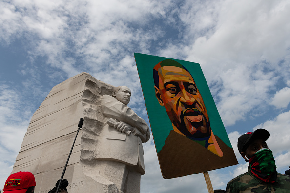 A demonstrator wearing a protective mask holds a painting of George Floyd at Martin Luther King Jr. memorial during the "Get Your Knee Off Our Necks" March on Washington in Washington, D.C., U.S., on Friday, Aug. 28, 2020. The civil rights rally will be headlined by the Reverend Al Sharpton and is expected to bring thousands to the site where Reverend Martin Luther King Jr. delivered his historic "I Have a Dream" speech 57 years ago.