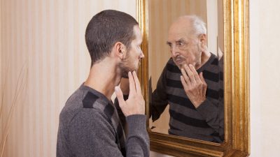 young man looking in mirror and old man looking in reflection