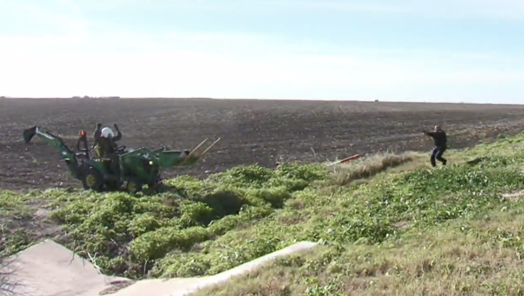 man on tractor with hands up and a police officer pointing a gun at him