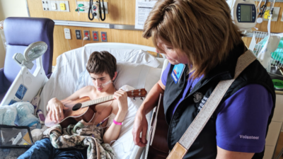 A musician plays with a child in a hospital bed