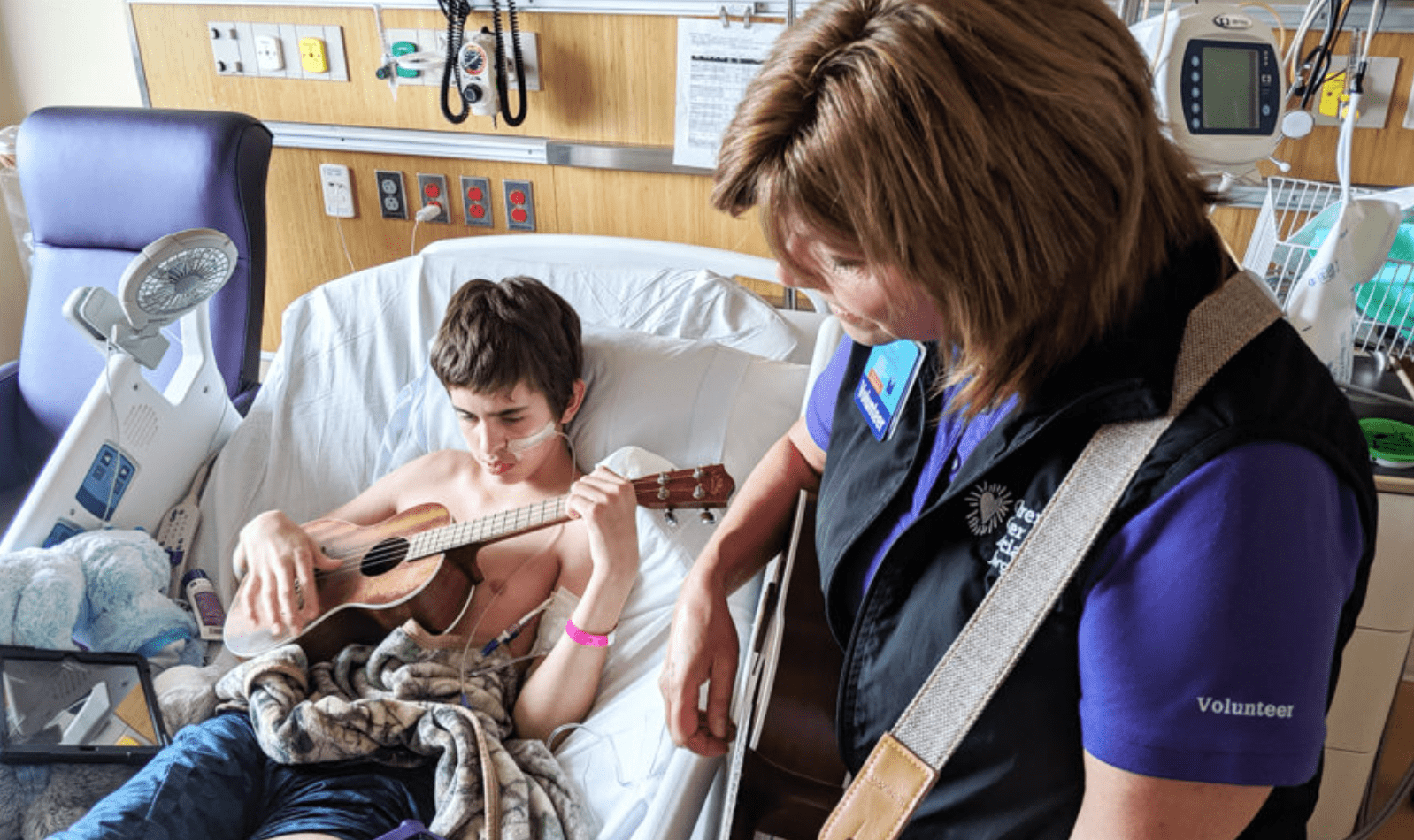 A musician plays with a child in a hospital bed