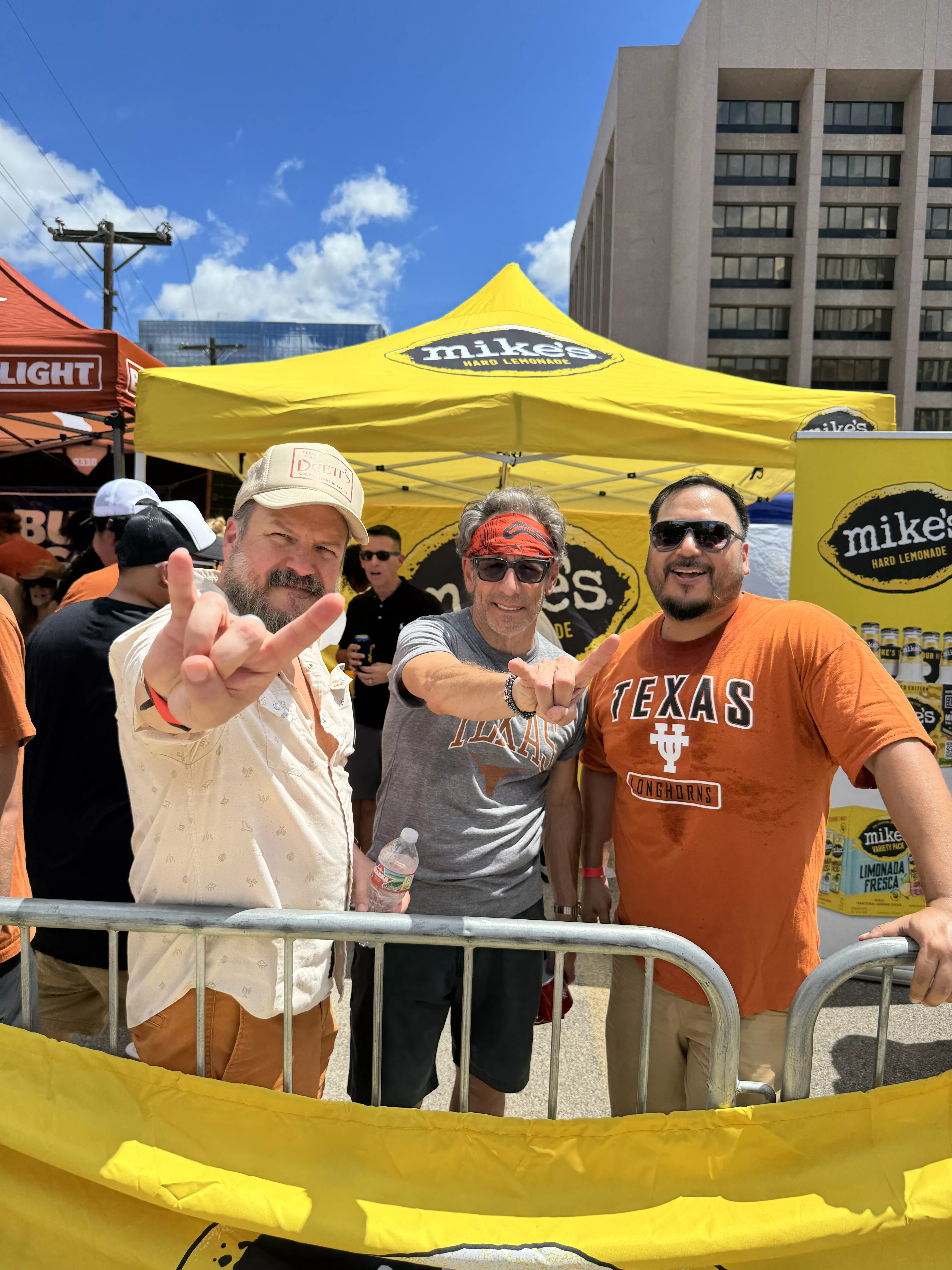 KLBJ FM Tailgate photo from 2024 Austin, Texas Matt, bob and Chuy pose for a photo in front of the Mike's Hard Lemonade Tent at Tailgate in September, 2024