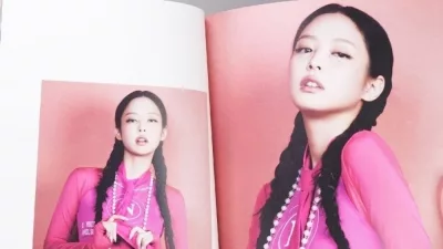 Fan hands holding BlackPink BORN PINK 2nd Album photobook with Jennie on grey. Pink music CD in player. South Korean girl group BlackPink