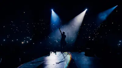 View from the stage stadium. Vocalist of a popular pop band on the background of the flashlights of phones during a concert. Fans switch on lights on smart phones on tribunes. Crowd waving cellphones