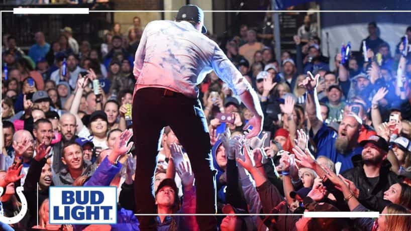 artist singing on stage leaning over to grab hand of audience member, colts logo, bud light logo