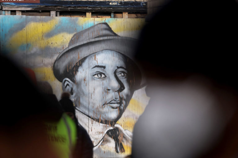 CHICAGO, ILLINOIS - JANUARY 19: A mural featuring a portrait of civil rights icon Emmett Till looks out from an abandoned building front as volunteers gather nearby with family members of Tamiko Talbert-Fleming after passing out flyers in the Chicago Lawn neighborhood seeking information about her murder on January 19, 2022 in Chicago, Illinois. Talbert-Fleming, a beautician, was shot and killed as she sat in her car after arriving for work on January 14. Till, a Chicago native, was 14-years-old when he was murdered while visiting family in Mississippi. His death and his mother's decision to have an open-casket service to show the brutality of the murder is credited with spawning the modern civil rights movement.