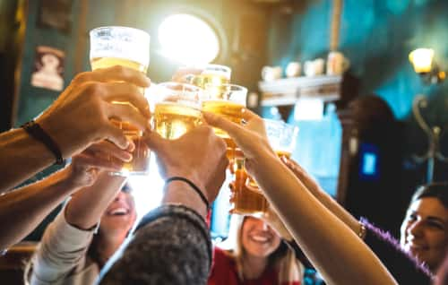 group of friends cheering with alcoholic drinks at a bar