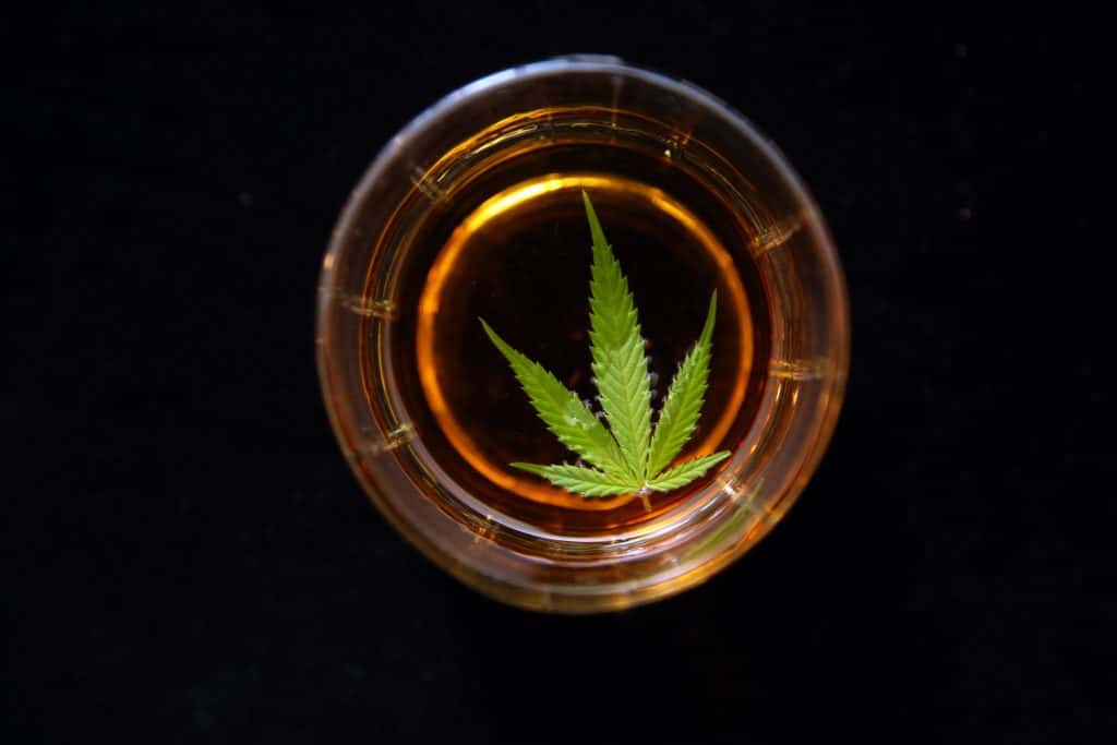 Cannabis leaf floating in a glass of liquor on a black velvet background