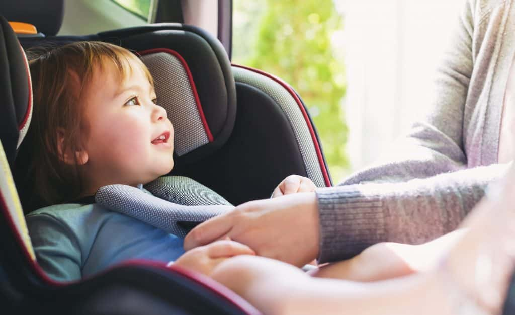 toddler being buckled into car seat