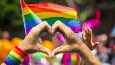 Hands in shape of heart in front of gay pride flag