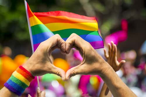 Hands in shape of heart in front of gay pride flag