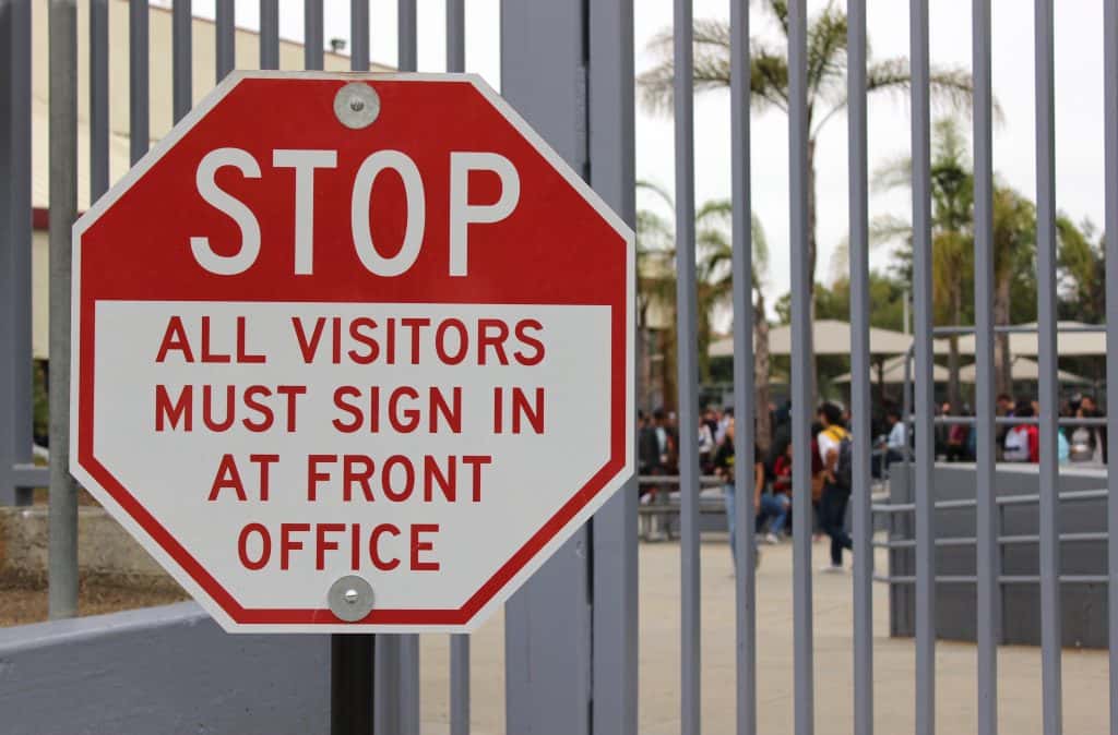 Stop sign that reads "STOP: all visitors must sign in at front office"