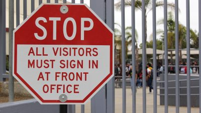Stop sign that reads "STOP: all visitors must sign in at front office"
