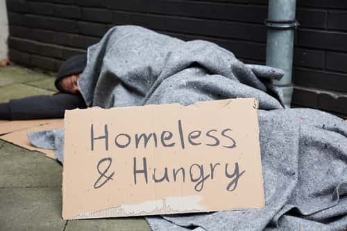 Homeless man on street with sign that reads "homeless and hungry"