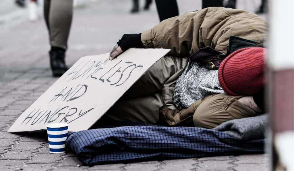 Homeless man on street with sign that reads "homeless and hungry"