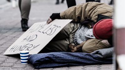 Homeless man on street with sign that reads "homeless and hungry"