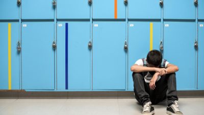 student sitting with head down in front of lockers