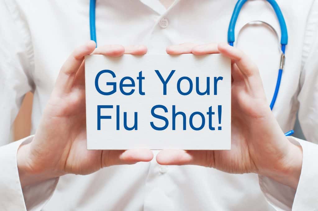 A nurse holding up a sign that says "Get Your Flu Shot."