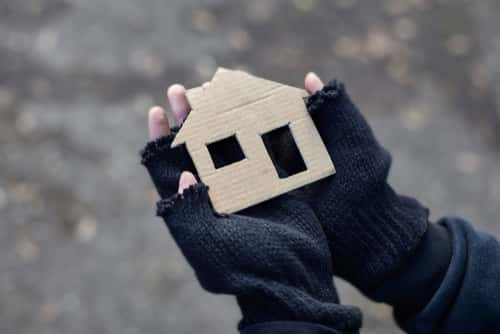 homeless man holding cardboard cut out of a house