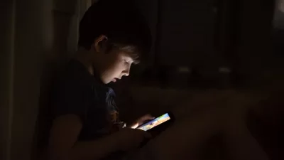 Kid who plays games on the internet at night. Portrait of a teenager boy using mobile phone on dark room