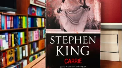 Paperback cover of Carrie by Stephen King shown on a bookshop shelf background