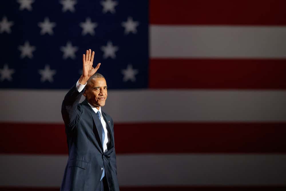 Barack Obama waving in front of American flag