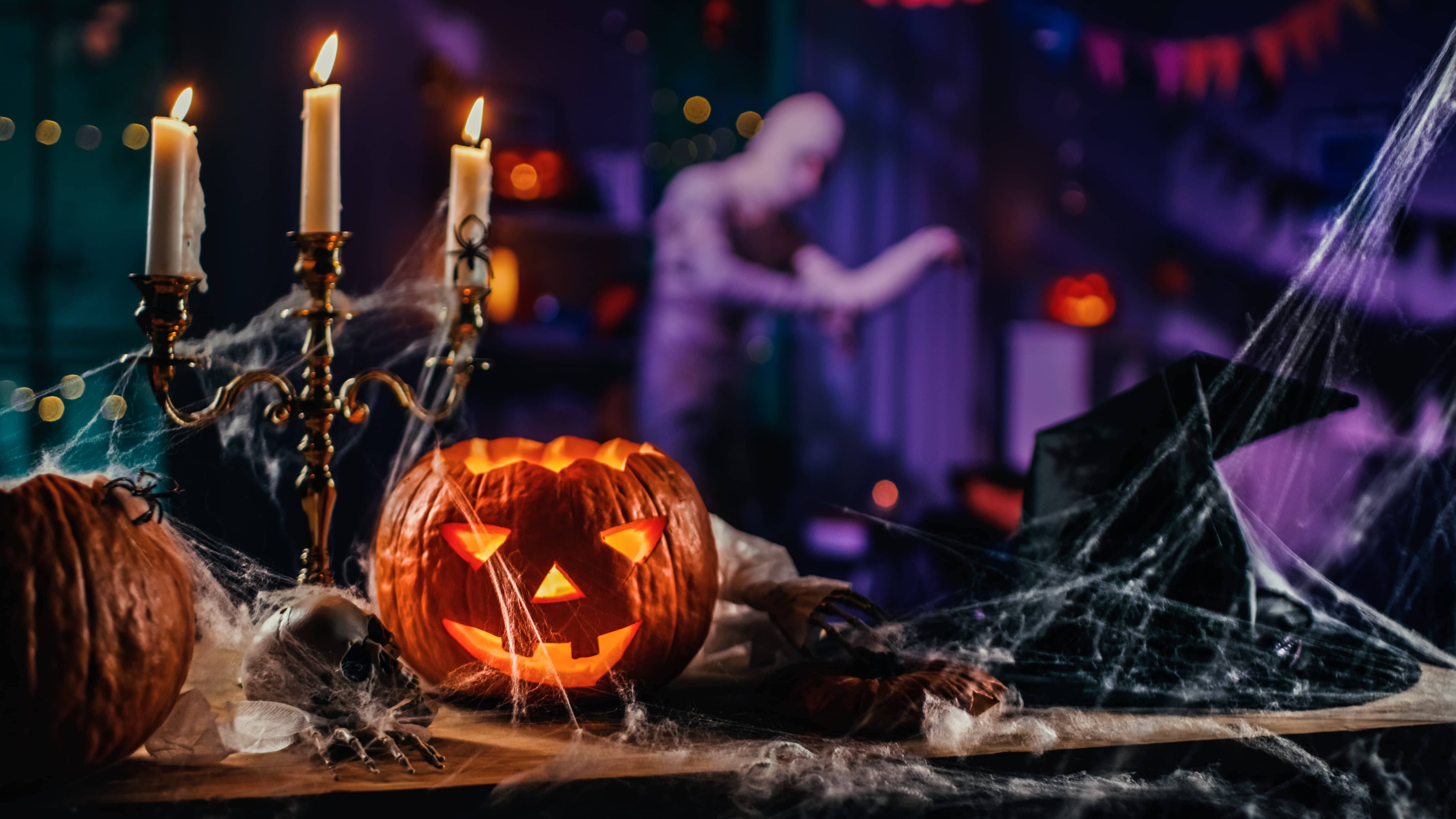 Halloween Still Life Colorful Theme: Scary Decorated Dark Room with Table Covered in Spider Webs, Burning Pumpkin, Candlestick, Witch's Hat and Skeleton. In Background Silhouette of Monster Walking By