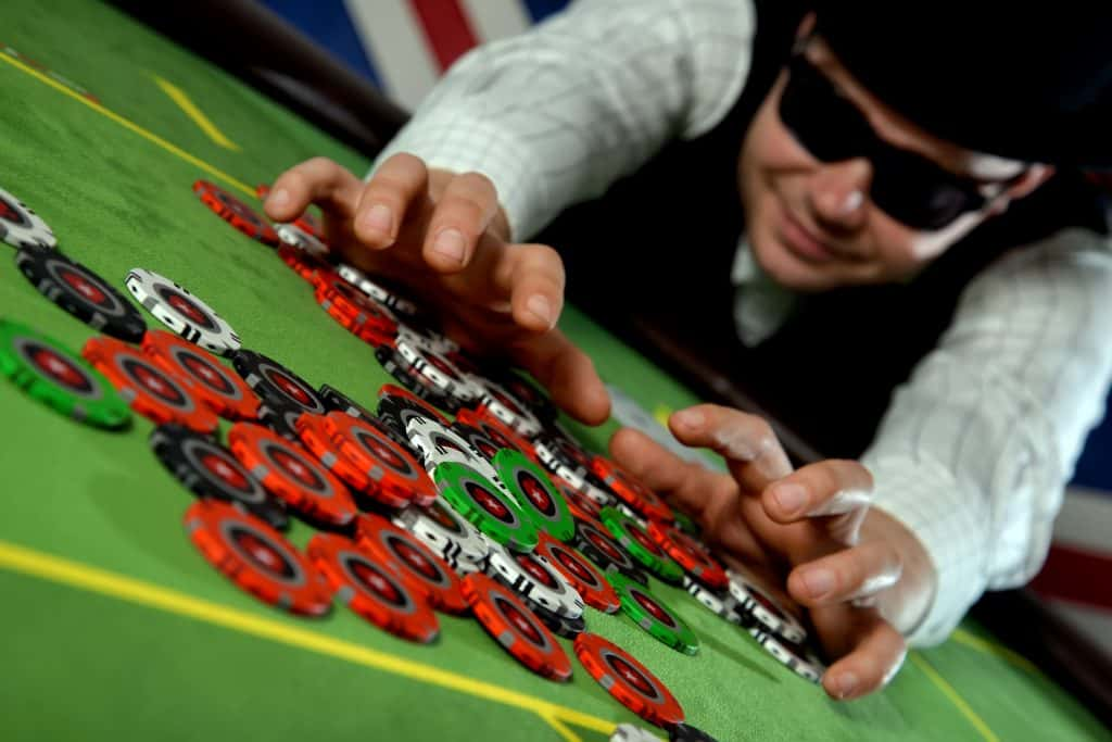 A man with a black hat and sunglasses collecting a pile of poker chips.