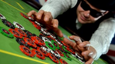 A man with a black hat and sunglasses collecting a pile of poker chips.