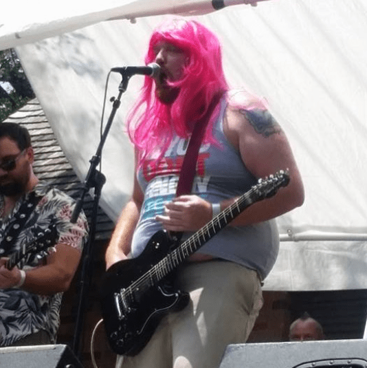 Jason playing the guitar in a pink wig.