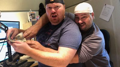 Nick reaching around from behind Jason to grab money from out of Jason's hands