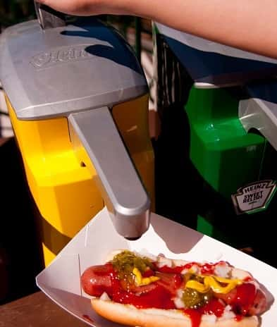 Fan dispensing mustard on his hot dog next to a concession stand at Giants baseball game.