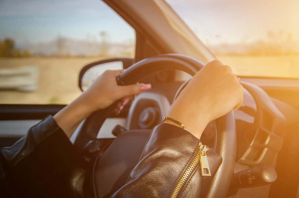 A lady with hands on the steering wheel.