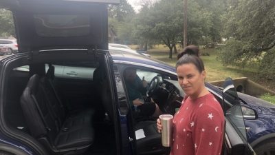 Deb making a mad face in front of Jason's Tesla.