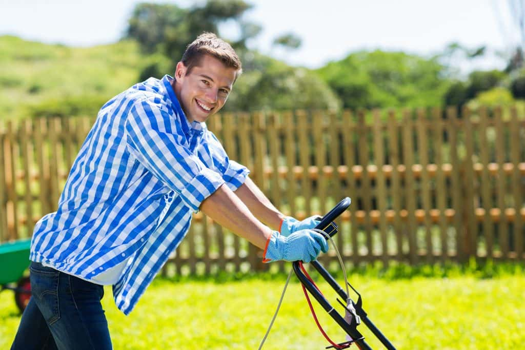 A man smiling and mowing the lawn.