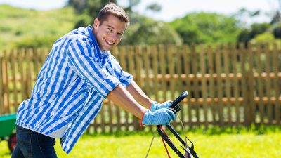A man smiling and mowing the lawn.