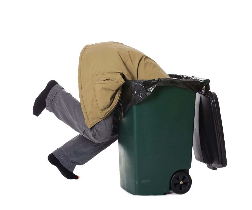 A guy diving with his head in a dumpster.