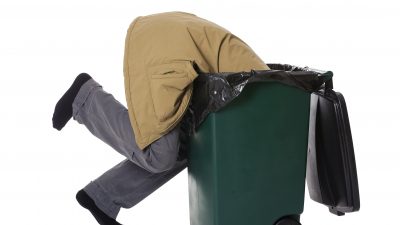 A guy diving with his head in a dumpster.