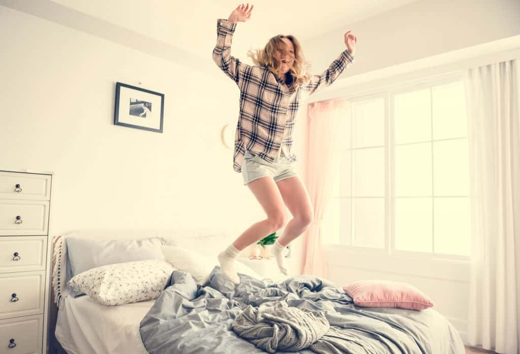 Image of a woman jumping on bed in shorts and a flannel top.