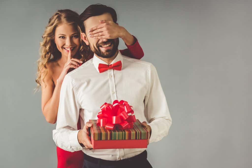 Lady covering a guy's eyes with a gift.