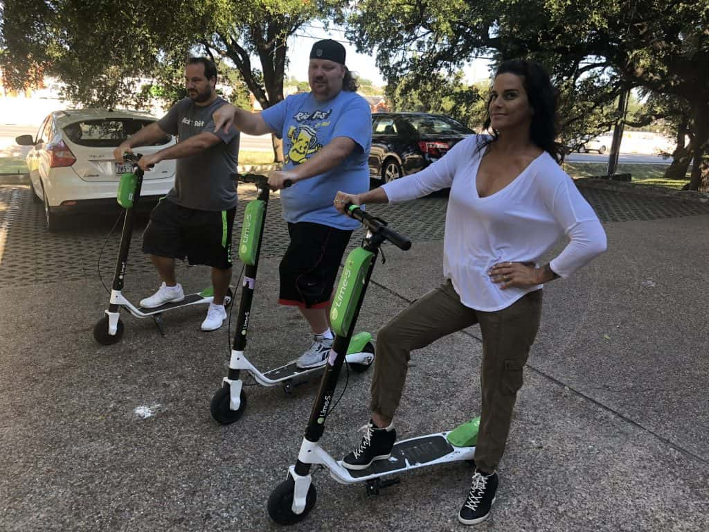 Jason, Deb and Nick ride lime scooters in front of the Emmis Austin parking lot