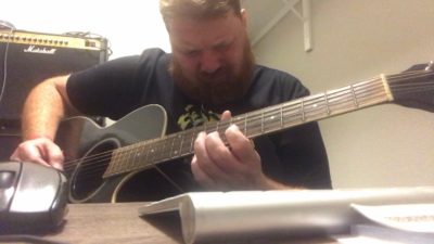jason dick playing an electric guitar in side his home studio/closet