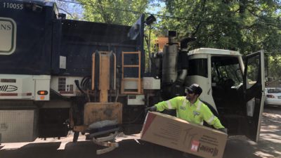 a garbage man throwing a cardboard box into a garbage truck