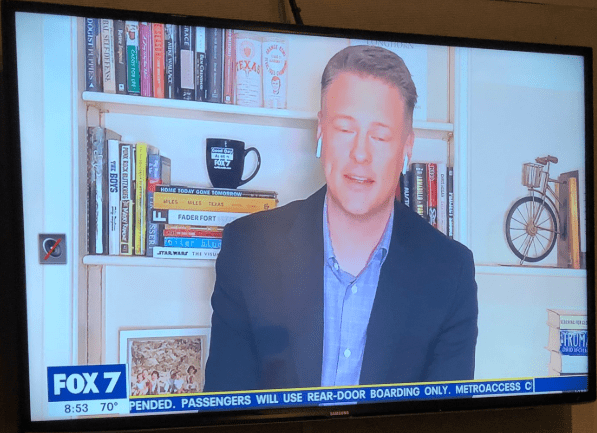 Fox 7 news anchor Dave Froehlich broadcasting from home in front of unleveled shelves