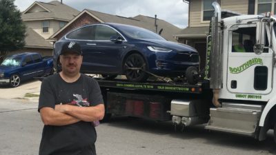 Jason looking agitated in front of his tesla being loaded onto a tow truck