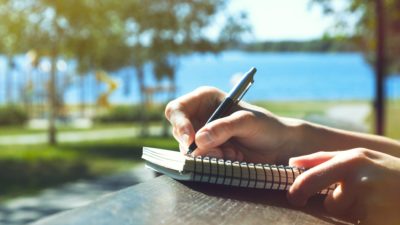 a stock photo of someone writing in a diary outside