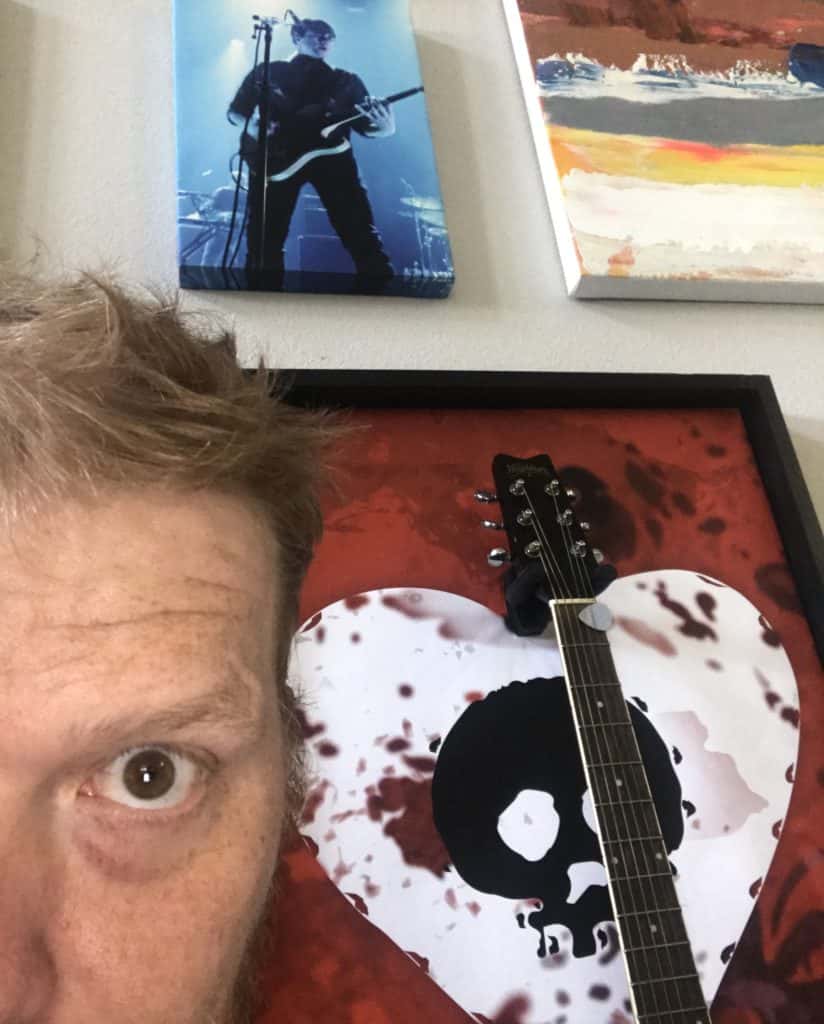Half of jason's face in front of a picture on his wall of jim atkins of jimmy eat world